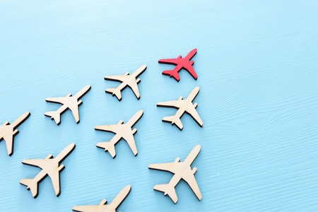 Leadership concept with airplanes on blue wooden background. One red leader flays ahead others.