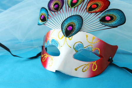 Photo of elegant and delicate venetian mask with peacock tail decoration element over turquoise silk backgroundの写真素材