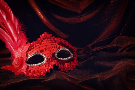 Photo of elegant and delicate red Venetian mask over dark velvet and silk backgroundの写真素材
