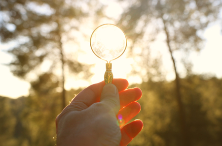 A male's hand holding a magnifying glass against the setting sun outside. Concept of search, creative thinking and use of solar energyの写真素材