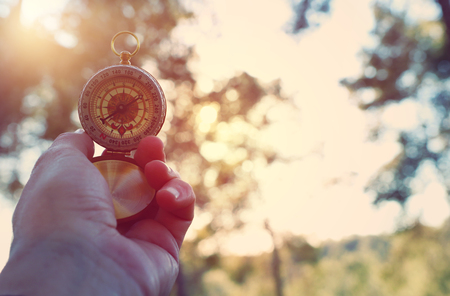 Male's hand holding a compass during travel in the forestの写真素材