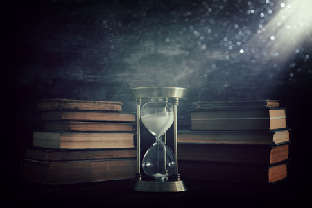 Hourglass as time passing concept and old books in front of black wall background. Conceptual photo on history, fantasy and education.の写真素材