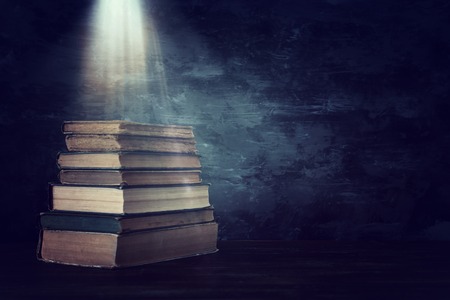 Stack of antique books with magical light on old wooden table. Fantasy medieval period and religious...