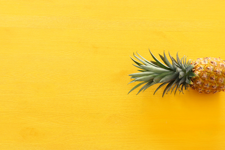 Ripe pineapple over yellow wooden background. Beach and tropical theme. Top view