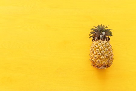 Ripe pineapple over yellow wooden background. Beach and tropical theme. Top view