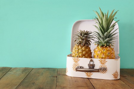 Ripe couple pineapple in suitcase over wooden table or deck. Tropical summer vacation concept
