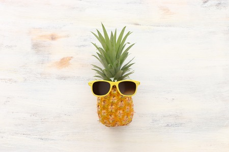 Ripe pineapple in stylish sunglasses over wooden white background. Tropical summer vacation concept....