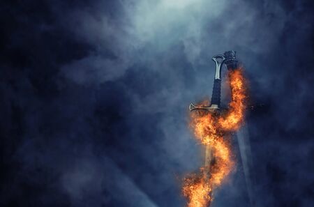 Mysterious and magical photo of silver sword with fire flames over Gothic black background. Medieval period conceptの写真素材