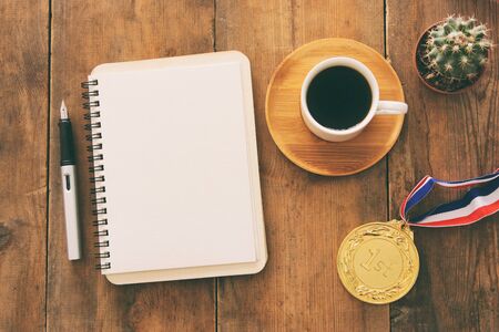 Open notebook with empty pages and other office supplies over wooden old office desk table. Top...