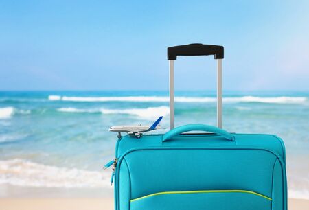 Holidays. Travel concept. Blue suitcase and airplane toy in-front of tropical sea backgroundの写真素材