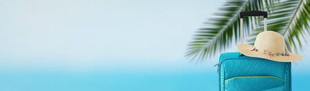 holidays. travel concept. blue suitcase with female hat infront of tropical background. bannerの写真素材