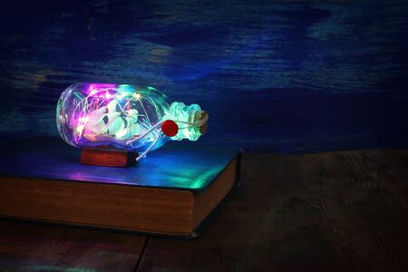 vintage sail boat in the bottle and garland lights over wooden table. Selective focus. nautical concept imageの写真素材