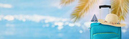 holidays. travel concept. blue suitcase with female hat and sailing boat infront of tropical background. bannerの写真素材