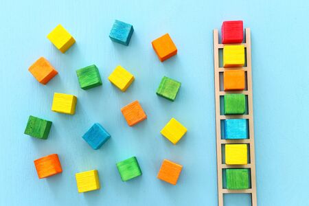 Business image of wooden ladder with colorful cubes over blue table, human resources and management...