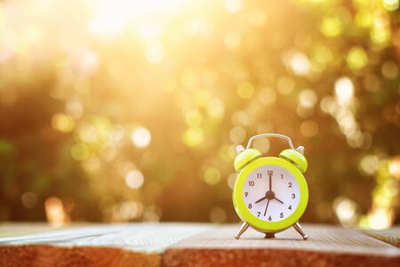 Image of autumn Time Change. Fall back concept. Dry leaves and vintage alarm Clock on wooden table outdoors at afternoonの写真素材