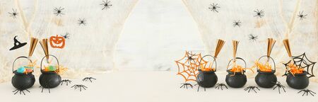 holidays image of Halloween. Witcher cauldron, broom, candies and spiders over white wooden table. bannerの写真素材