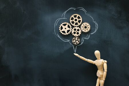 Wooden dummy holding sign with cogweels . New idea concept or choosing the right solutionの写真素材