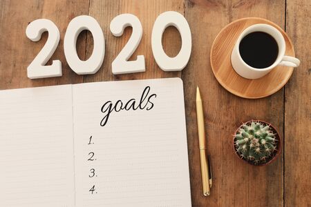 Business concept of top view 2020 goals list with notebook, cup of coffee over wooden desk