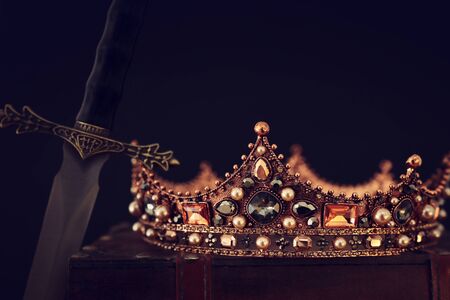 low key image of beautiful queen/king crown over antique box next to sword. fantasy medieval period. Selective focusの写真素材