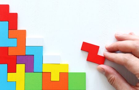 man's hand holding a square tangram puzzle, over wooden tableの写真素材