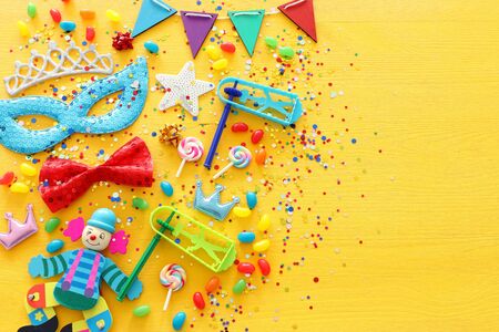 Party colorful noisemaker, mask and cute clown doll over yellow wooden background . Top view, flat layの写真素材