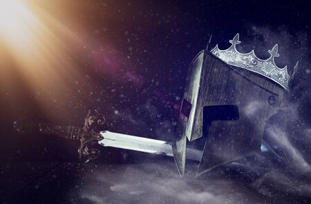 photo of crown over king knight helmet armor and sword over dark background. Medieval period conceptの写真素材