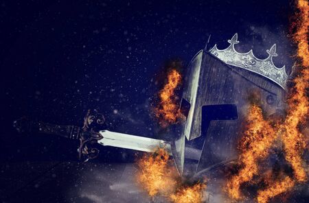 photo of crown over king knight helmet armor and sword in front of fire flames and dark background....