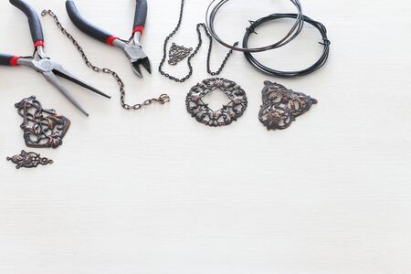 Jewellery making concept with cooper chain, filigree charms and tools over white wooden background