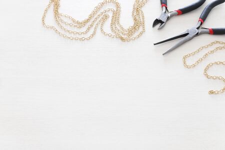 Jewellery making concept with gold chain and tools over white wooden background
