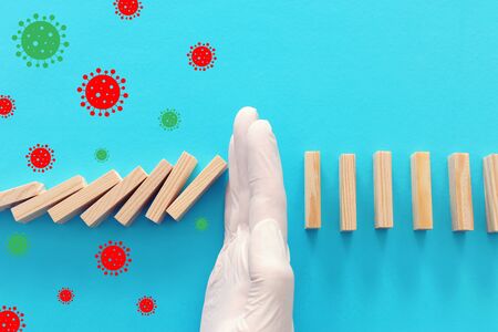 a male hand in glove stopping the domino effect. covid 19 or coronavirus blocking concept