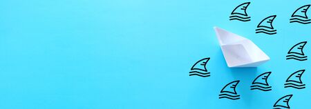 concept image of avoiding crisis. paper boat escaping sharks idea