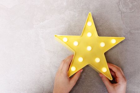 Child holding yellow plastic star with lights bulbs over pastel background