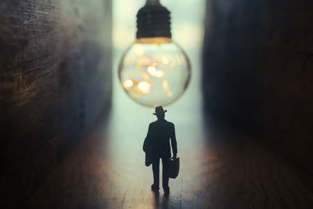 Surreal image of person in dark corridor looking at glowing light bulb. Concept of finding the right idea, or way outの写真素材