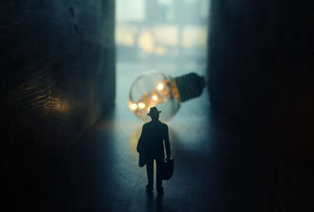 Surreal image of person in dark corridor looking at glowing light bulb. Concept of finding the right idea, or way outの写真素材