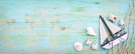 nautical concept with white decorative sail boat, seashells over blue wooden background