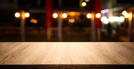 background Image of wooden table in front of abstract blurred restaurant lightsの写真素材