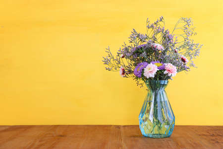 bouquet of colorful field flowers in the glass blue vase over wooden tableの写真素材