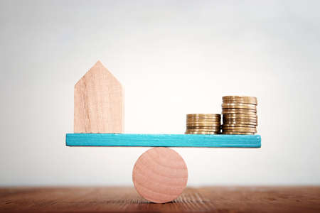 Concept image of small house and stack of coins balancing on seesawの写真素材