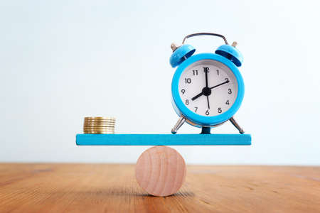 Stack of coins and vintage clock balance on seesaw