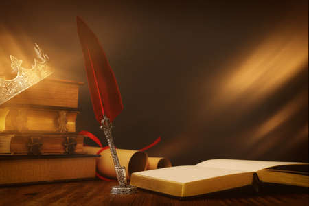low key image of beautiful queen/king crown over old book and feather quill ink pen over wooden table. fantasy medieval periodの写真素材