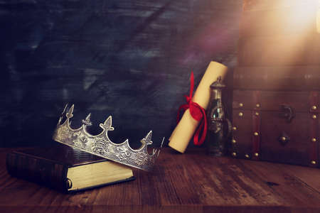 low key image of beautiful queen/king crown, old books and feather quill ink pen over wooden table. fantasy medieval periodの写真素材
