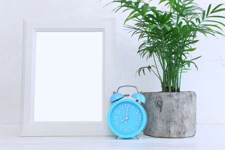 Image of white empty photo frame next to home plant over wooden table. For mockup, can be used for...