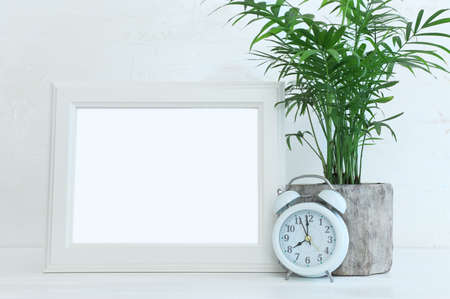 Image of white empty photo frame next to home plant over wooden table. For mockup, can be used for photography montage and textの写真素材