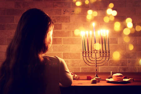 Low key image of jewish holiday Hanukkah background with girl looking at menorah (traditional candelabra) and burning candlesの写真素材