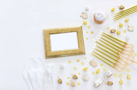 Image of jewish holiday Hanukkah with menorah (traditional Candelabra), donut, wooden dreidel (spinning top). Coronavirus prevention concept, medical mask and and sanitizer gelの写真素材