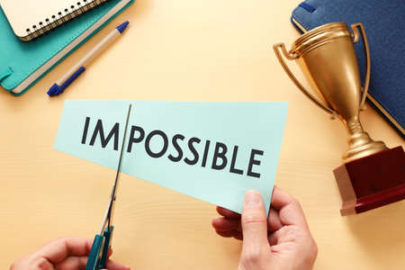 man hand holding card with the text impossible, cutting the word im so it written possible. success...