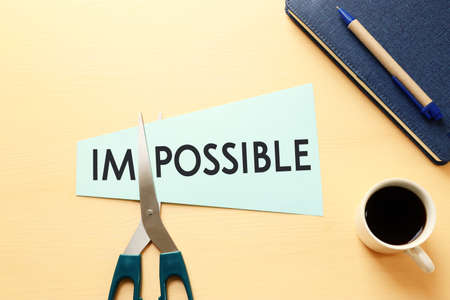 man hand holding card with the text impossible, cutting the word im so it written possible. success and challenge concept.の写真素材