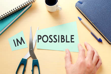 man hand holding card with the text impossible, cutting the word im so it written possible. success...