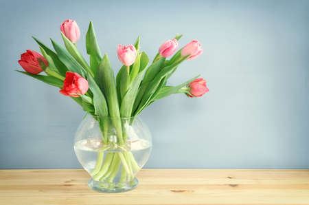 spring bouquet of red and pink tulips flowers in the glass vase over wooden tableの写真素材