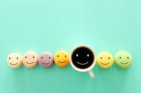 cup of coffee and colorful macaroon with happy face on wooden mint backgroundの写真素材